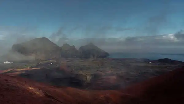 Red and green mountains are being seen from heights, with the ocean in the background